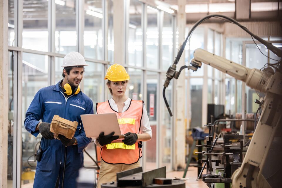 Engineer and worker control and check robot working in factory. The worker is controlling the robot to work in the factory