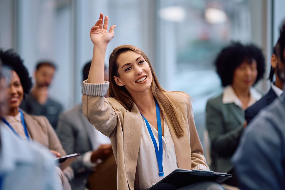 Happy entrepreneur raising her arm to ask question during business conference in board room