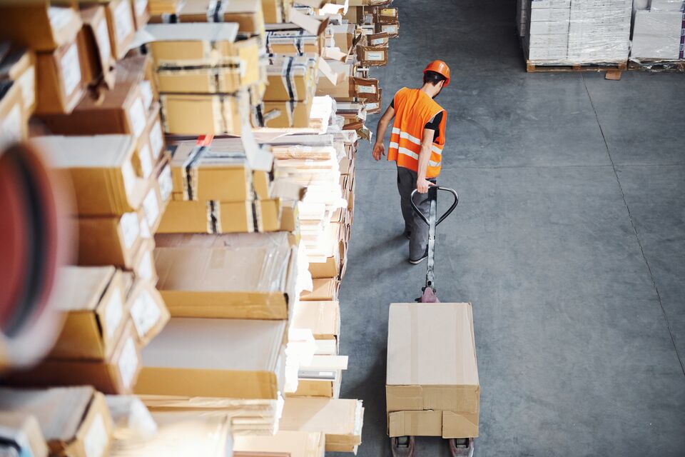 Young male worker in uniform is in the warehouse pushing pallet truck