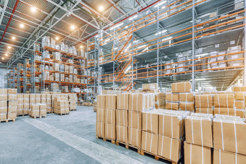 Large industrial warehouse with high racks. In the foreground are a lot of cardboard boxes