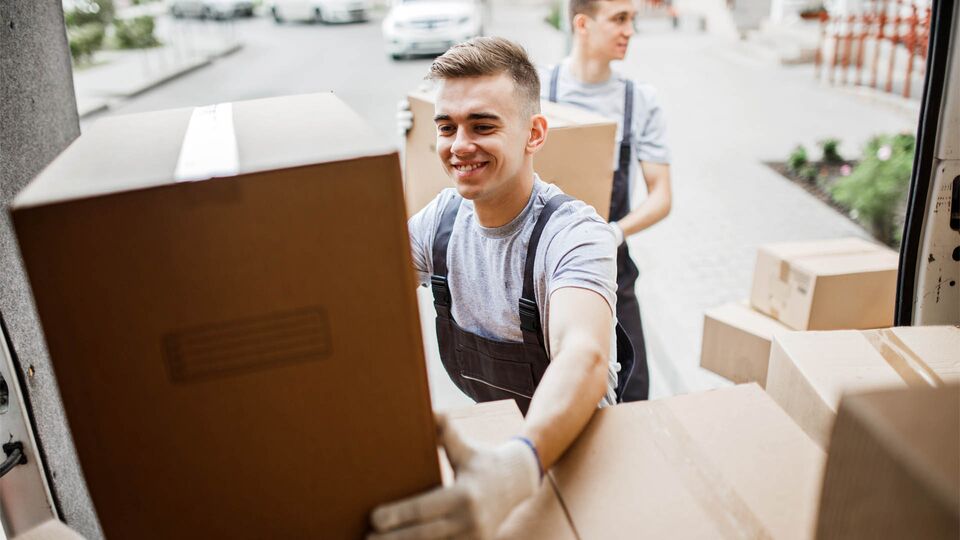 A young handsome smiling mover wearing uniform is reaching for t