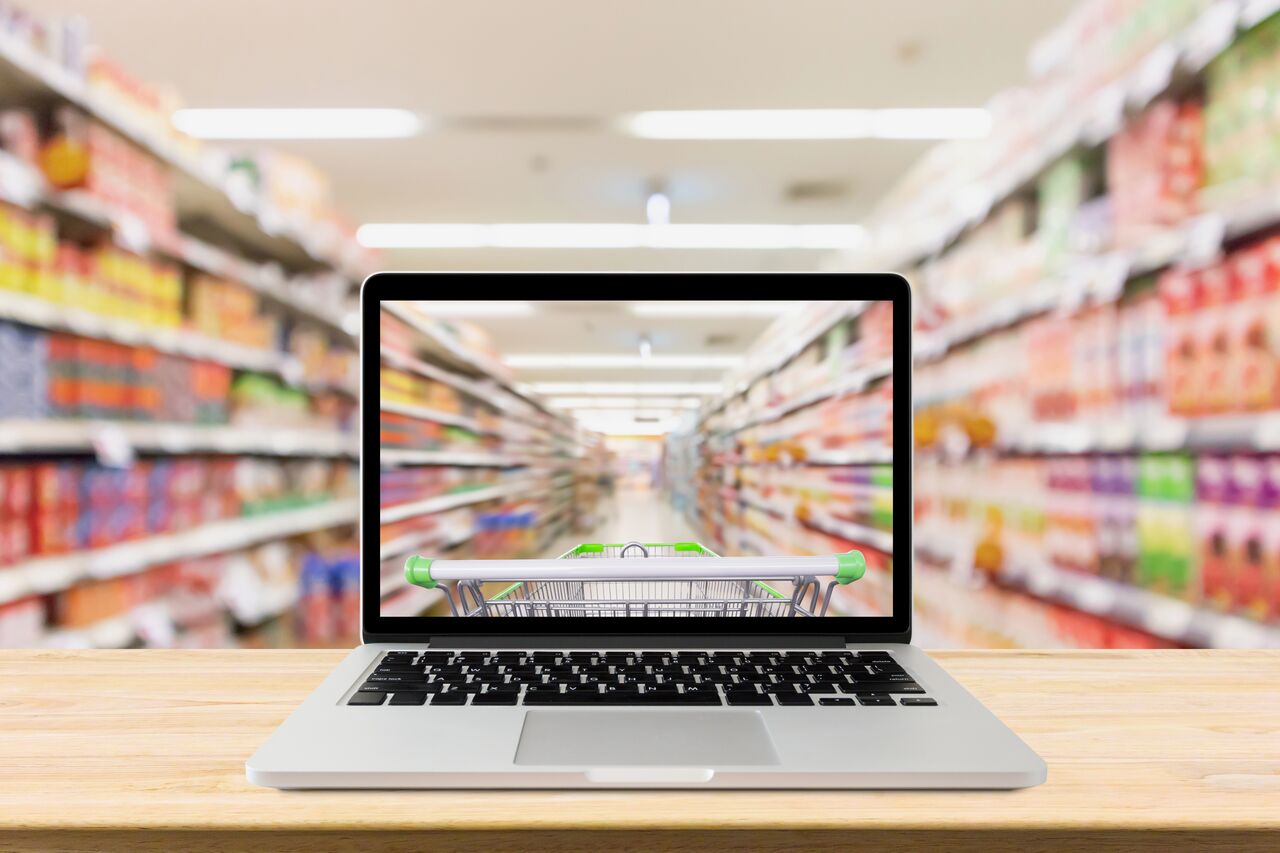 laptop computer on wood table with supermarket aisle blurred background online shopping concept