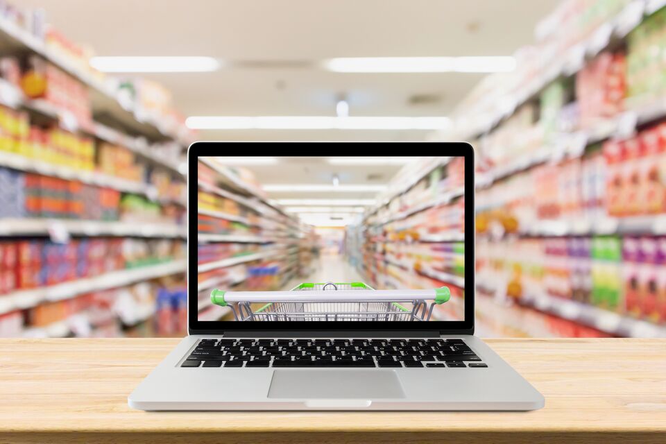 laptop computer on wood table with supermarket aisle blurred background online shopping concept
