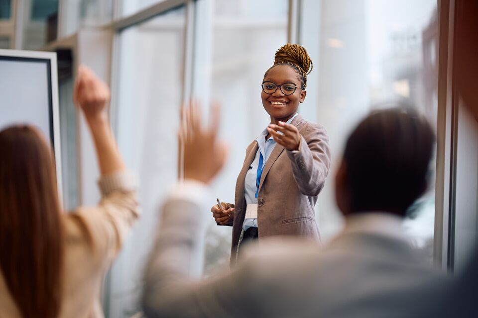 Happy black business seminar speaker pointing at attendee who wants to ask question in conference room.
