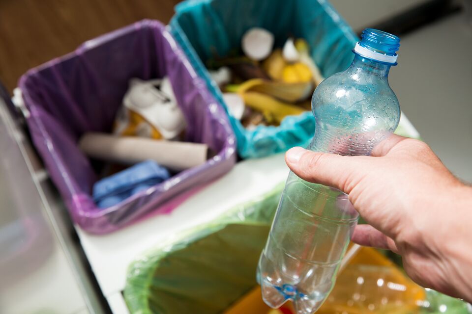 Man putting empty plastic bottle in recycling bin in the kitchen. Person in the house kitchen separating waste. Different trash can with colorful garbage bags. top view